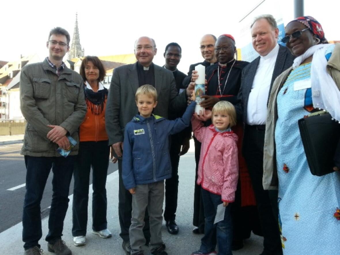 Dekan Ulrich Kloos übergibt auf der Ulmer Herdbrücke die missio-Kerze an Kardinal Philippe Ouédraogo.
