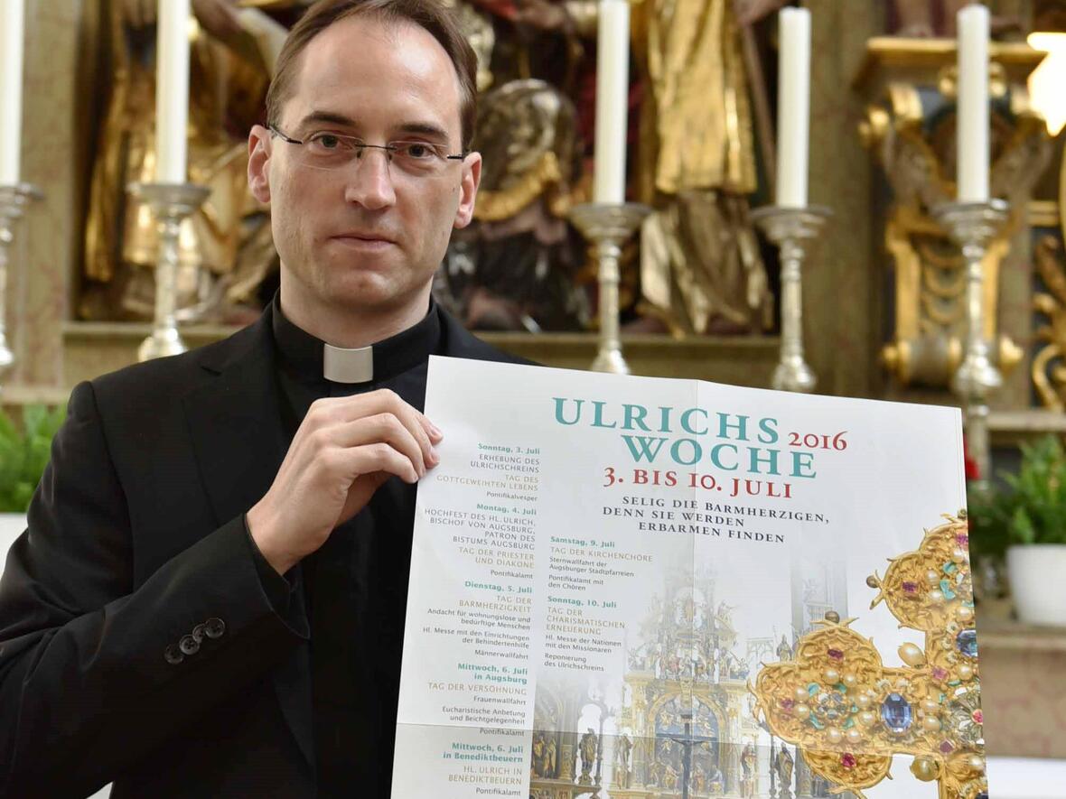 Stadtpfarrer Christoph Hänsler präsentiert das Plakat der diesjährigen Ulrichswoche. (Foto: Pressestelle Bistum Augsburg/Maria Steber)
