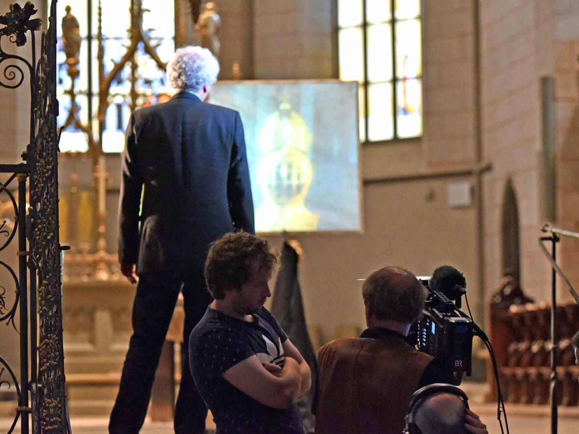 Das Team vom Bayerischen Fernsehen gemeinsam mit Schauspieler und Sprecher Udo Wachtveitl bei den Dreharbeiten zur Dokumentation im Augsburger Dom. Der Sprecher richtet seinen Blick auf den Funeralhelm Karls V., der im Hintergrund auf die Leinwand projiziert ist. (Foto: Nicolas Schnall / pba)