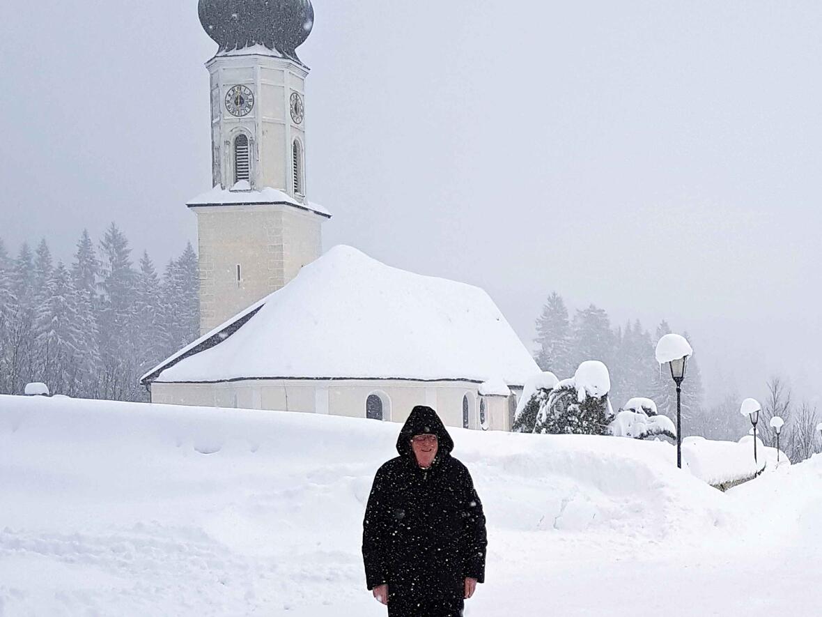 Nimmt die Situation mit Humor und einer gesunden Portion Gelassenheit: Pfarrer Willi Milz vor seiner von Schneemassen umgebenen Pfarrkirche St. Nikolaus. (Foto: privat)