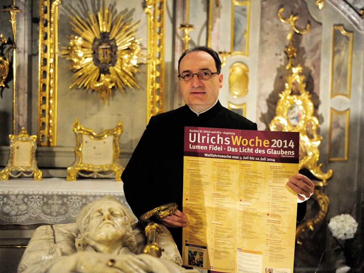 Stadtpfarrer Lothar Hartmann mit dem Plakat zur Ulrichswoche am Grab des hl. Ulrich (Bild: pba/Nicolas Schnall).