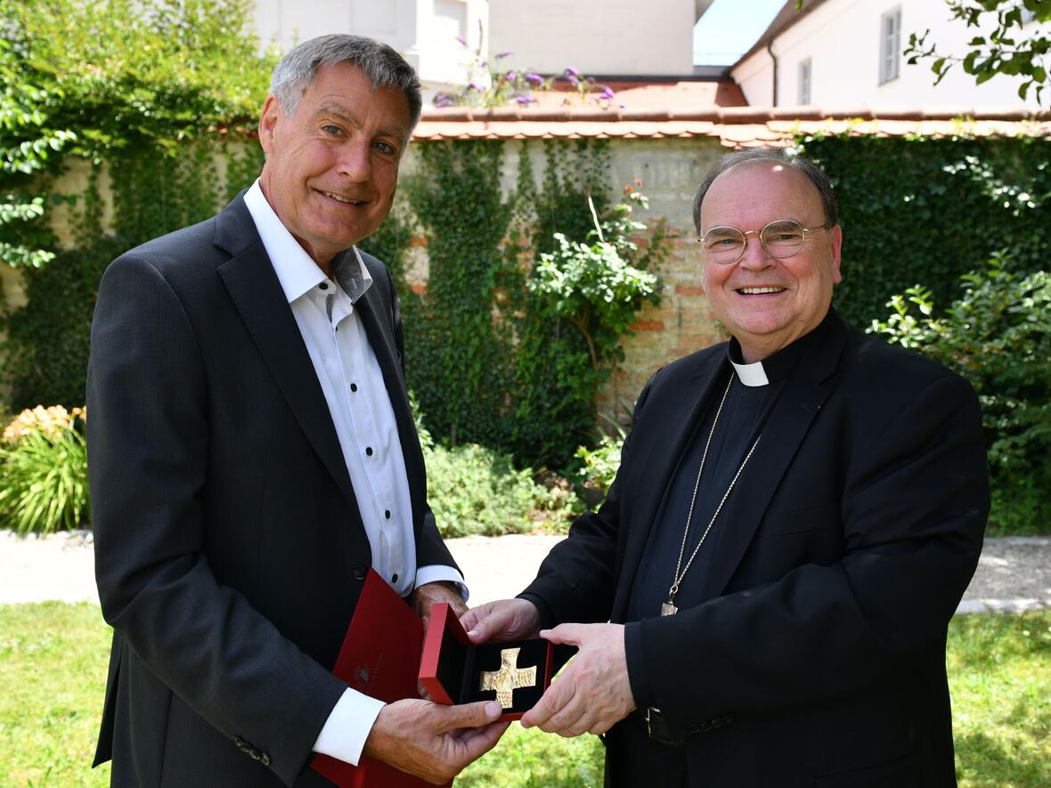 Bischof Bertram überreicht das Ulrichskreuz in Gold an den ehemaligen Geschäftsführer des Sankt Ulrich Verlags Johann Buchart (Foto: Julian Schmidt / pba)