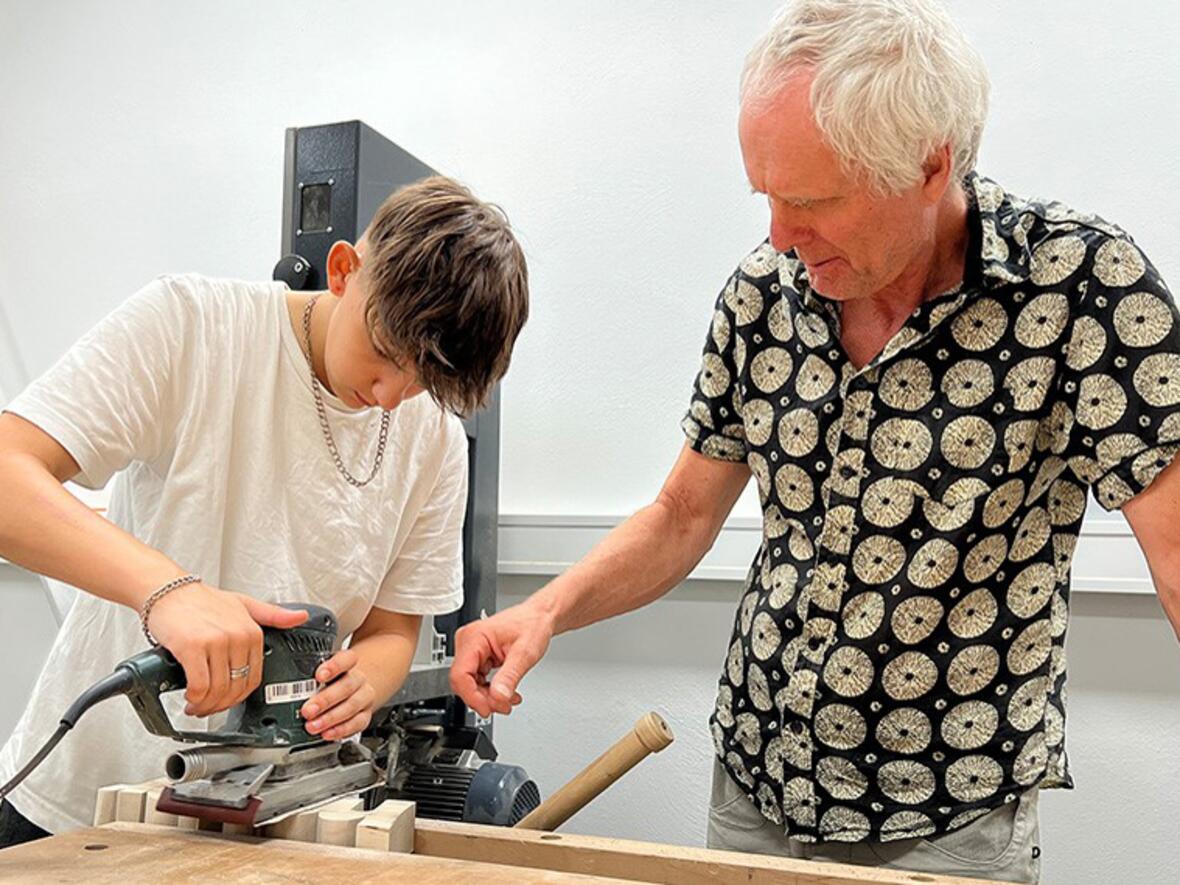 Mit Methoden der Kunst- und Werkpädagogik können sich die Schulverweigernden der „Schule in der Werkstatt" als leistungsfähig erleben. Ein Schüler probiert sich mit Hilfe des KJF Mitarbeiters und Künstlers Gerhard Fauser an der Schleifmaschine. (Foto: KJF Augsburg / Christina Bauer)