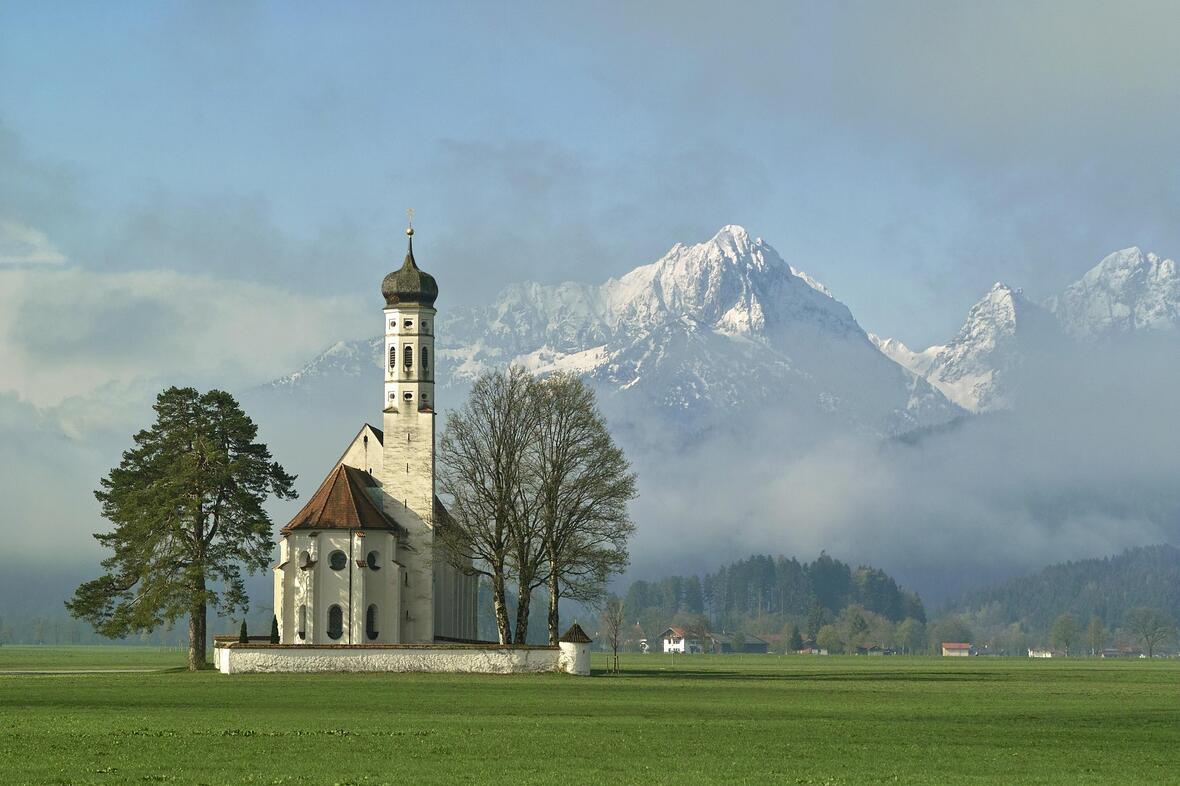 Die Kirche Sankt Coloman in Schwangau vor einer traumhaften Bergkulisse. (Motivbild: pixabay)