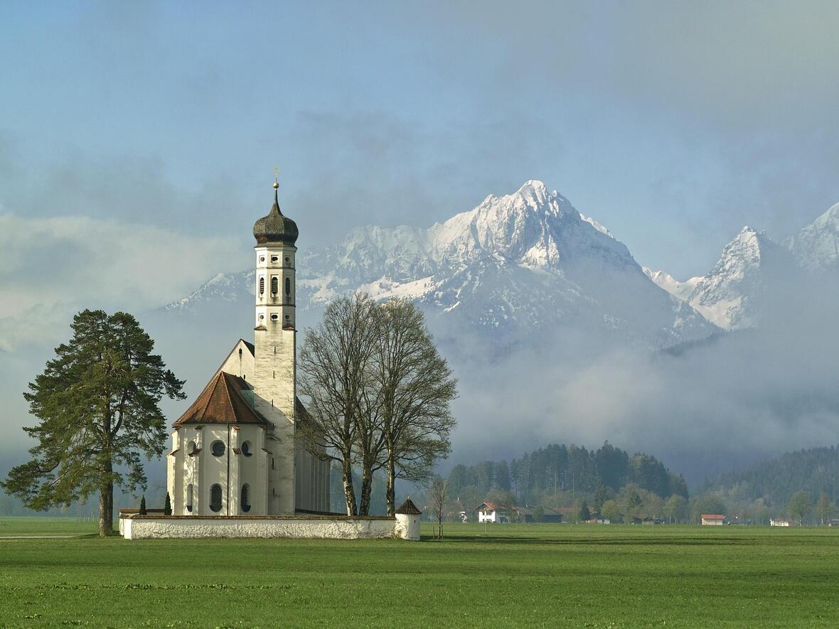 Die Kirche Sankt Coloman in Schwangau vor einer traumhaften Bergkulisse. (Motivbild: pixabay)